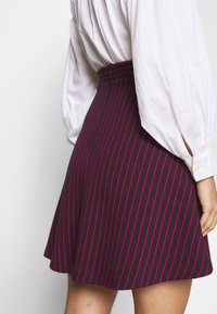 Marineblauwe rok met rode verticale strepen, uitlopende vorm, zacht aanvoelende stof, en voorzien van een hoge taille met een ritssluiting aan de achterkant.