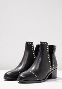 Black leather ankle boots with low block heels, decorated with silver studs along the edges and toe cap.