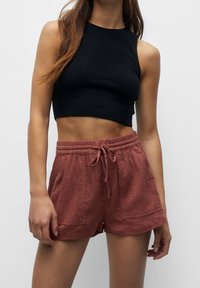 Zwarte geribde crop top gecombineerd met roestkleurige, gestructureerde shorts met een elastische tailleband en trekkoord, zijzakken en een losse pasvorm.