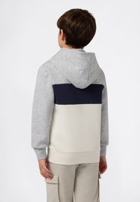 Niño de espaldas que lleva una sudadera con bloques de color: mangas grises, parte superior trasera en azul marino y parte inferior trasera en beige. También viste pantalones cargo beige con bolsillos.