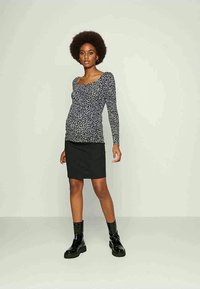 Camisola de mangas longas com padrão de bolinhas pretas e brancas, combinada com uma saia mini preta ajustada; modelo a usar botins pretos robustos.