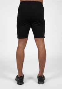 Zwarte sportieve shorts met een elastische tailleband, strakke pasvorm, gladde textuur en geen zichtbare patronen. Gew worn met zwarte hardloopschoenen.