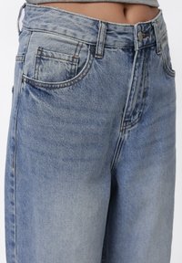 Lys blå denim jeans med høy midje, med frontlommer, synlig søm og en lett falmet tekstur.