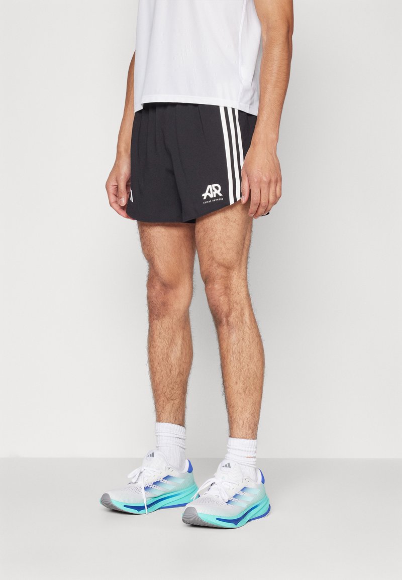 Shorts de sport noirs avec des rayures blanches, logo à l'avant, associés à des chaussures de course blanches et aqua avec un mesh texturé et une semelle rembourrée.