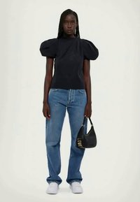 Top nero con maniche a sbuffo, jeans blu a gamba dritta, sneaker bianche, tiene una borsa nera con la scritta "LOVE" stampata in oro. Design semplice e moderno.