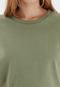 Khaki zelené tričko s kulatým výstřihem, vyrobené z měkké látky; má hladký povrch a jednoduchý design bez vzorů nebo akcentů.