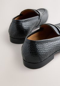 Schwarze Loafers aus strukturiertem Leder mit glatter Sohle und abgerundeter Spitze, verziert mit Ziernähten und einem schlanken Design.