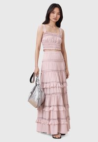 Lyserød cropped top med flæsekant, sat sammen med en lagdelt maxikjole. Glat stof, minimalistisk sølvhandtaske og sorte sandaler.