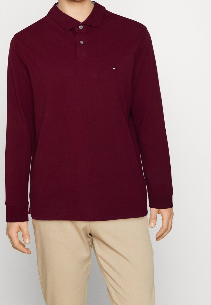 Burgundy langærmet polo-shirt lavet af bomuld. Har en klassisk krave, tre knapper og et lille logo på brystet. Tilpasset pasform.