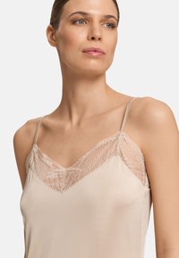 Camiseta beige con tirantes finos, que presenta un encaje en el escote y una textura suave y lisa en toda la tela.