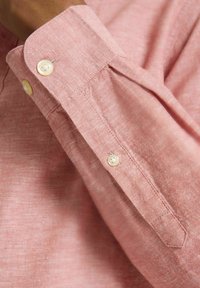 Puño de camisa de lino rosa claro con dos botones crema, textura sutil y un diseño clásico con detalle plegado en la manga.
