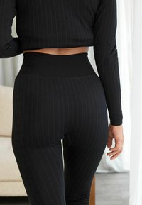 Sorte ribbede leggings med høj talje, features vertikale striber og en tætsiddende design. Stoffet ser strækbart og struktureret ud.