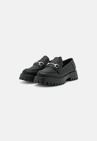 Mocasines de cuero negro con una plataforma gruesa y suela estriada, con acentos de hebilla plateada en la parte frontal. Textura suave en toda su superficie.