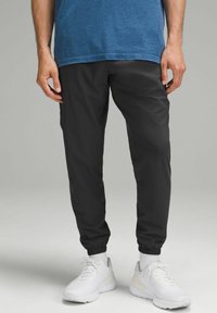 Sorte joggerbukser med elastiske manchetter lavet af letvægtsmateriale, parret med hvide sneakers og en blå struktureret kortærmet skjorte.