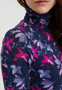 Närbild av en kvinna som bär en marinblå polotröja med rosa och lila blommönster.