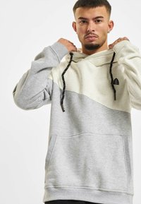 Hooded sweatshirt featuring gray and cream color block design, textured fabric, drawstring with black accents, and a front pocket.