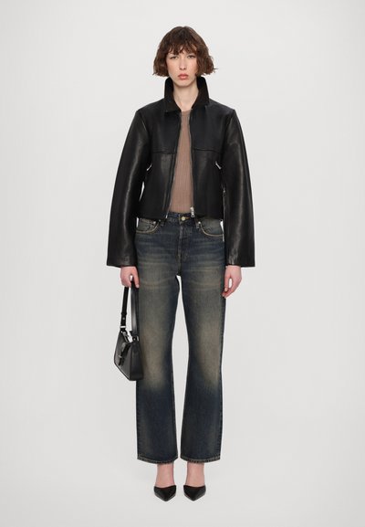 Svart läderkavaj med kort skärning och hög krage, parat med ljusblå slitna raka jeans. Modellen håller en liten svart handväska.