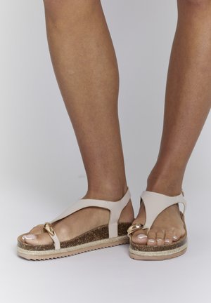 Lichtbeige sandalen met een gestructureerde kurken zool, met een V-vormig ontwerp en een goudkleurig rond hardware-detail op de bovenkant.