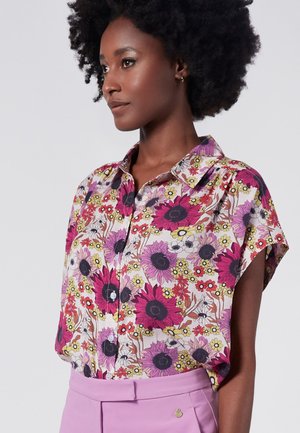 Blusa floreale in tessuto multicolore con fiori rosa, viola e bianchi con centri neri. Collo classico e maniche corte.