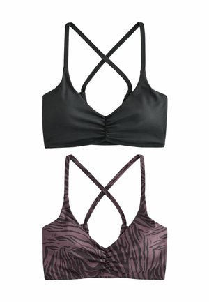 Due reggiseni sportivi con spalline incrociate sulla schiena, uno nero solido e uno viola con motivo astratto nero, distesi su sfondo bianco.