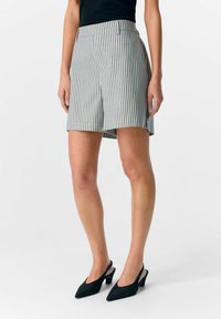 Stribede shorts i grå og hvidt stof med en flad talje, sidelommer og en design der slutter midt på låret. Sæt sammen med sorte stiletter.