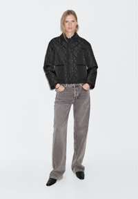 Quilted black jacket with snap closure and two pockets, paired with gray denim pants and black ankle boots. Smooth texture and structured design.