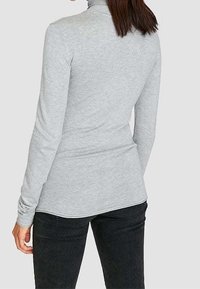 Szary, długi rękaw turtleneck z miękkiego materiału, o dopasowanym kroju i zakrzywionym dole, zestawiony z ciemnymi spodniami.