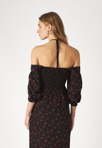 Abito nero off-the-shoulder con stampa floreale rossa, corpetto arricciato, maniche lunghe a sbuffo e un laccio al collo. Tessuto morbido e leggero.