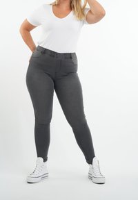 Leggings gris avec une taille élastique, design ajusté et détails de couture subtils, associés à un t-shirt blanc à col en V simple et des baskets blanches.