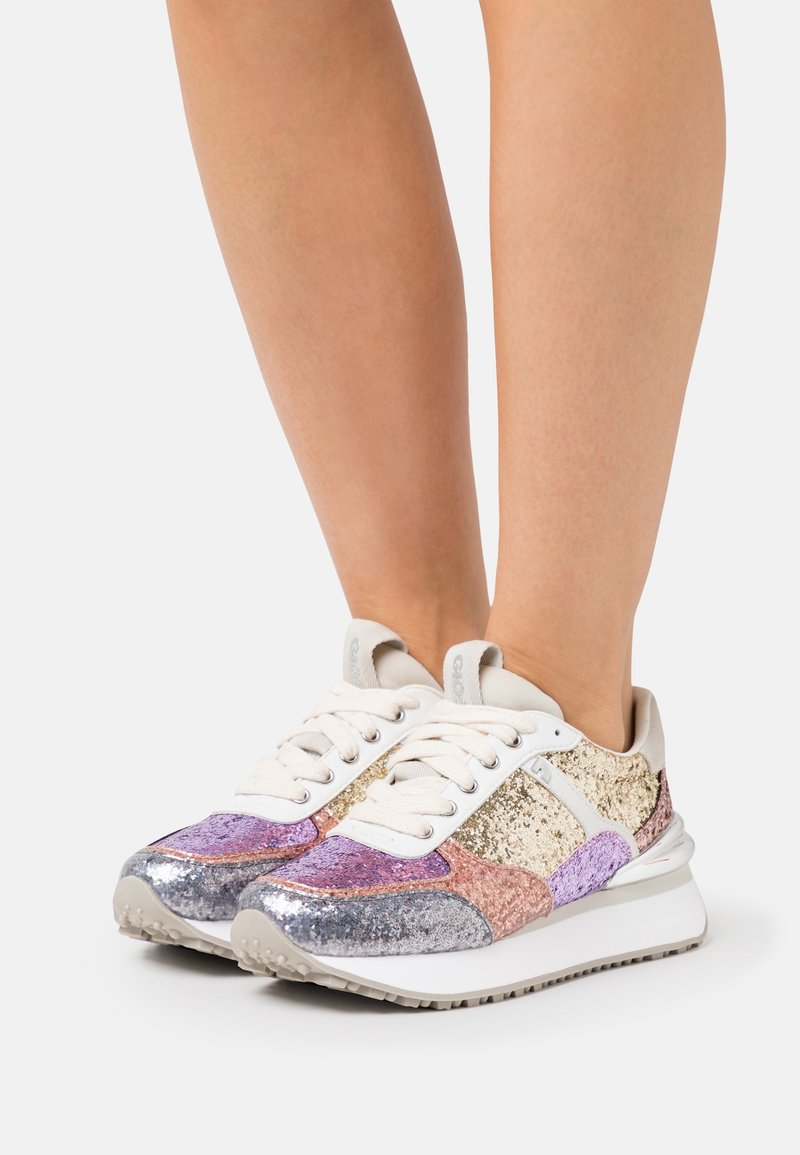 Femme portant des baskets pailletées multicolores en argent, or, rose et violet sur une semelle plateforme blanche.
