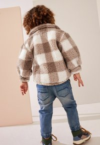 Fleecejakke i brun og hvid ternet mønster, med krave, oversized pasform, parret med lyseblå denimjeans og flerfarvede støvler.