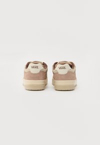 Adidași din suede maro cu accente bej, având guler căptușit, șireturi plate și talpă din cauciuc. Numele mărcii "VANS" este afișat pe spate.