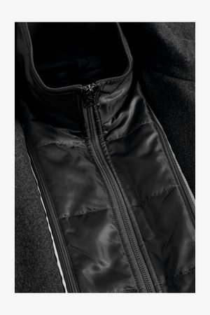 Mustat takit, joissa on sileä, pehmustettu sisävuori, etuvetoketju ja korkea kaulus, taustalla teksturoitu hiilenharmaa ulkokangas.