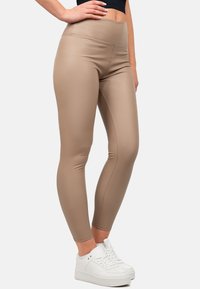 Leggings beige a vita alta realizzati in un materiale liscio e elastico, caratterizzati da una silhouette aderente e dettagli di cucitura sottili. Abbinati a sneakers bianche.