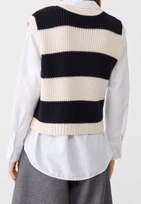 Gilet sans manches en tricot avec des rayures horizontales bleu marine et crème. Présente des bords côtelés, un tissu texturé et un design court.
