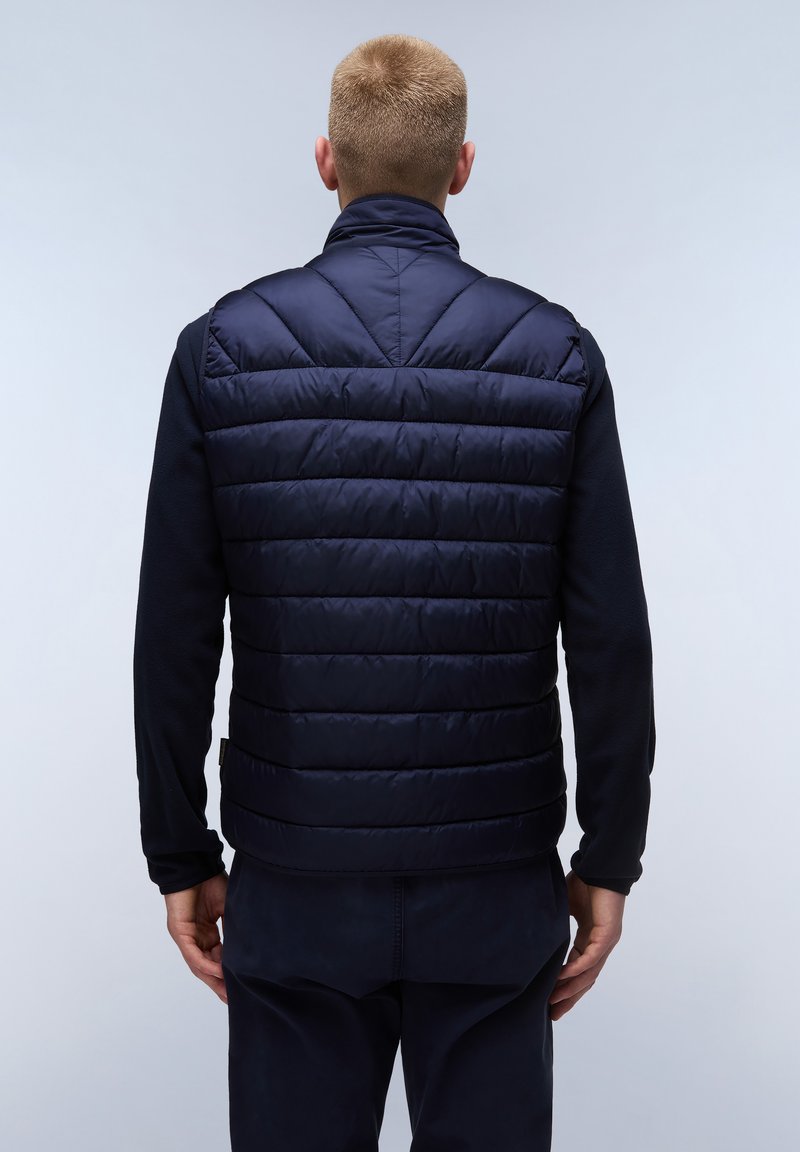 Gilet imbottito blu navy con design trapuntato, colletto alto e zip frontale. La vista posteriore mostra cuciture orizzontali e una texture morbida su una camicia tinta unita.