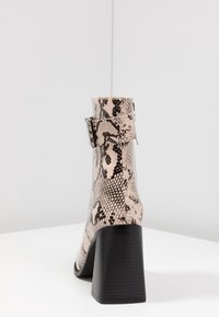 Stivale alla caviglia con tacco in pelle stampa serpente rosa e nera. Presenta un accento con fibbia e un tacco a blocco texturizzato. Finitura liscia con un design aderente alla caviglia.