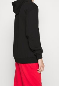 Sort hætte sweatshirt med ribbede manchetter og kant, har en afslappet pasform og blød tekstur; båret med røde løse bukser.