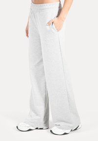 Pantalones deportivos gris claro de pierna ancha hechos de tela suave con cintura elástica y bolsillos laterales. Presentan una marca sutil en la pierna izquierda.