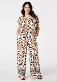 Ensemble deux pièces composé d'un haut à manches courtes et d'un pantalon large en tissu crème avec des motifs de feuilles bruns et noirs et des bordures décoratives.