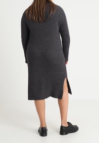 Dark gray ribbed knit dress with long sleeves, featuring a side slit and a fitted silhouette, paired with black platform shoes.