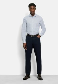 Himmelblaues kariertes Hemd mit langen Ärmeln, taillierte Passform. Getragen mit dunkelblauen Hosen und schwarzen Lederschuhen. Am Bund mit einem Gürtel gehalten.