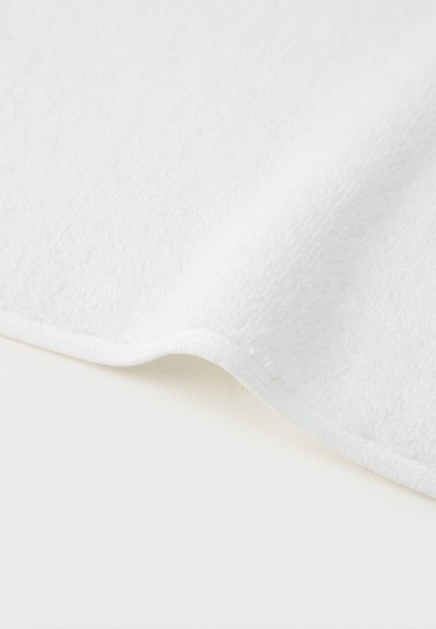 Απαλό λευκό ύφασμα φλις με ομαλή, ελαφρώς καμπυλωτή άκρη, που δείχνει υφή και λεπτή ραφή κατά μήκος του περιθωρίου.