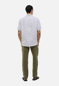 Chemise en lin blanche à manches courtes avec un empiècement arrière, associée à un pantalon en coton vert olive et des sandales noires. Tissu uni avec peu de détails.