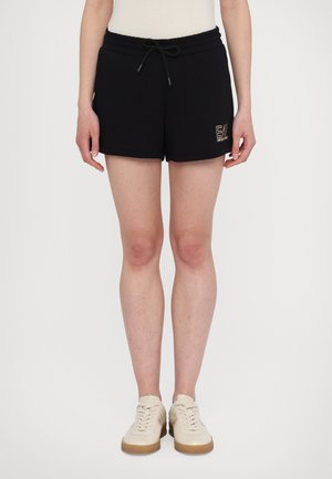 Sorte bomullsshortser med elastisk midje og snøring, med detalj av gulllogo på venstre side.