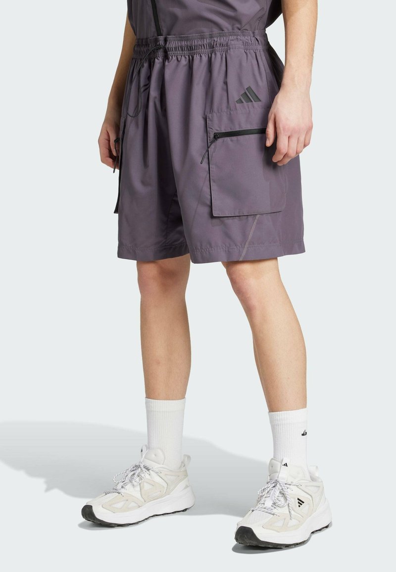 Lätta lila shorts för män med elastiskt midjeband, sidofickor och svarta blixtlåsdetaljer. Kombinerat med vita sneakers och strumpor.