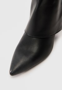 Close-up of the pointed toe and upper part of a black leather boot with visible stitching detail.