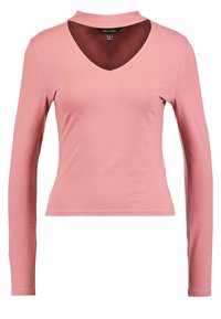 Langärmliges, eng anliegendes Oberteil aus weichem rosa Baumwollstoff mit tiefem V-Ausschnitt und hohem Kragen. Sanfte Textur mit minimalen Nähdetails.