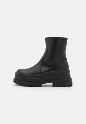 Schwarze Stiefeletten mit glattem Lederfinish, klobiger Plateausohle und strukturiertem Gummiprofil. Seitlicher Reißverschluss und abgerundete Zehenpartie.