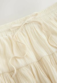 Primo piano di una vita elastica color crema con coulisse annodata su una gonna o pantaloni in tessuto leggero plissettato.